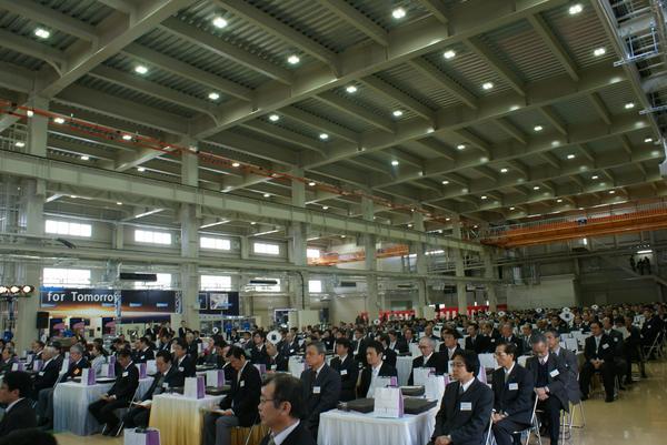 新工場竣工披露祝賀会でたくさんの出席者の方々が準備された机に座っている写真